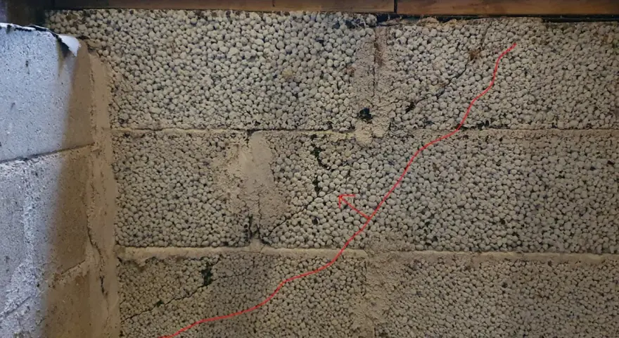 Synliga sprickor i grundmur av lättklinkerblock. En röd linje markerar en spricka som löper diagonalt över blocken.