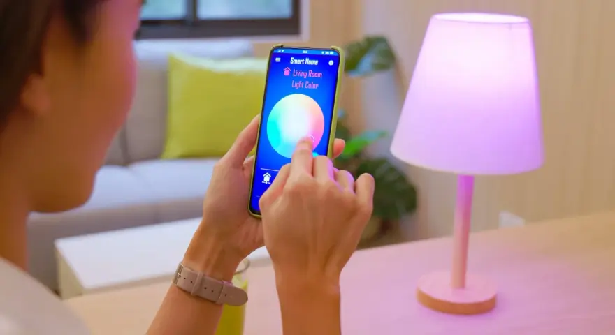 Person styr lampor med iPhone. Appen "Smart Home" visar färgval för vardagsrumsljuset.