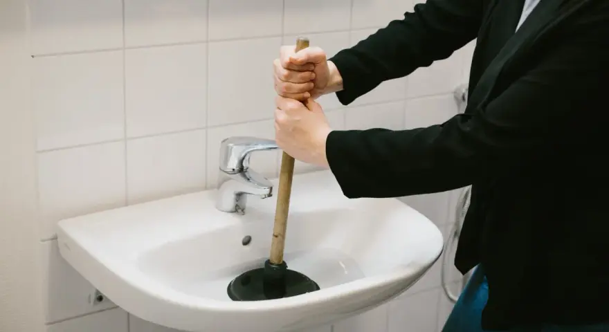 Person använder en sugpropp för att rensa vattenlås i handfatet.