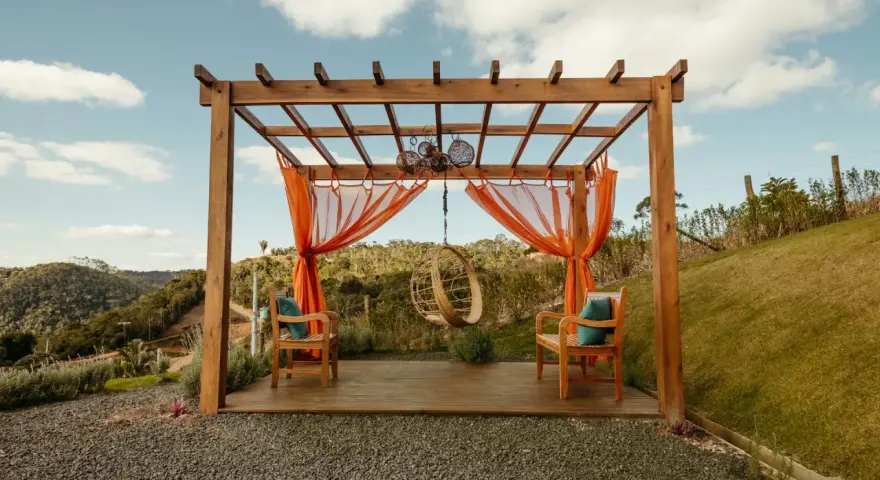 En vacker träpergola med orange draperier och hängstol. Perfekt för att bygga pergola på altan och njuta av utsikten.