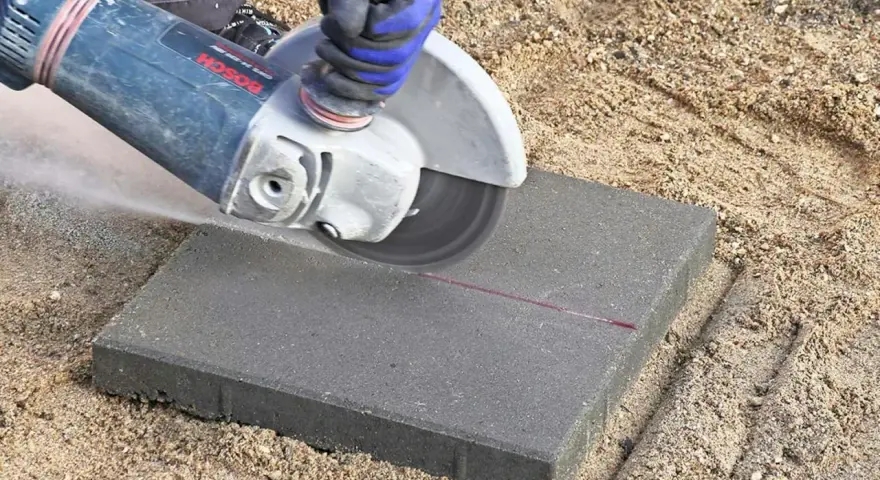 En person kapar marksten med en vinkelslip. Damm virvlar upp när stenen delas längs en markerad linje.