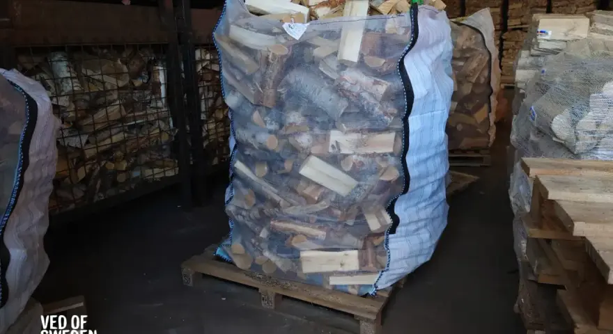 Stor säck med ved på pall, redo att stapla. Veden är kluven och förpackad för leverans.