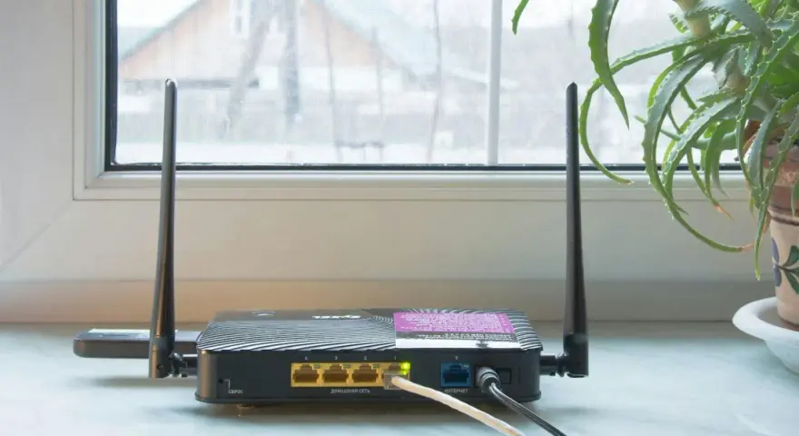 En gammal router med två antenner står på en fönsterbräda. En aloe vera-växt syns till höger.