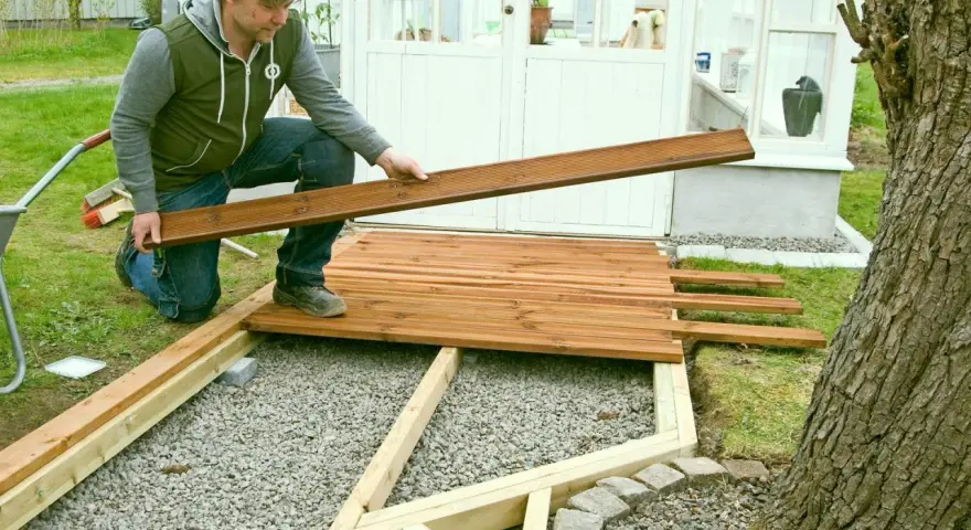 Man bygger trall vid ett växthus. Han håller en träbräda redo att läggas på plats.