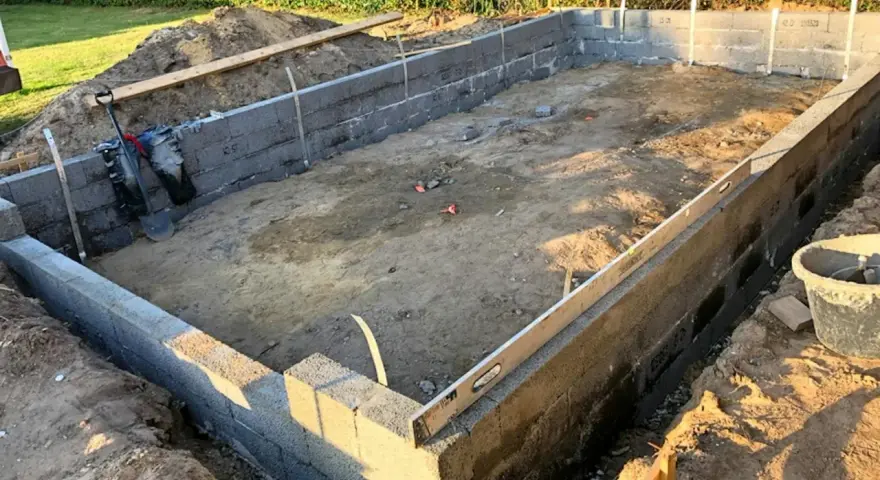 Byggarbetsplats med ett mura grund av betongblock. Schakt, spade och vattenpass syns.