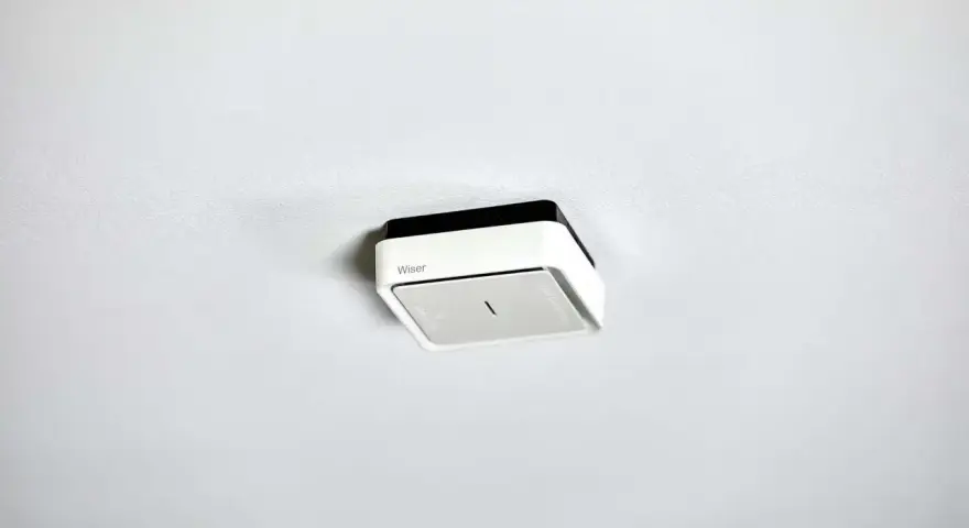 En vit och svart brandvarnare från Wiser monterad i taket. Denna brandvarnare utan batteri är redo att installeras.