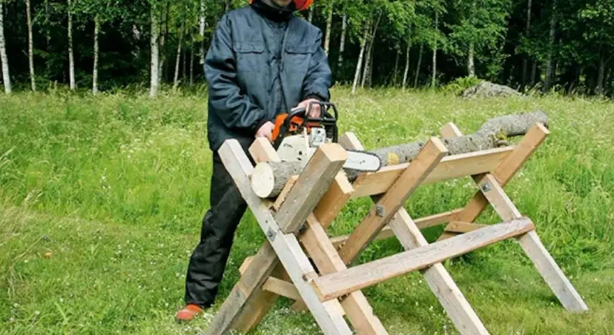 Man i skyddsutrustning använder motorsåg för att kapa ved på en sågbock. Ritning av en sådan konstruktion kan vara användbar.