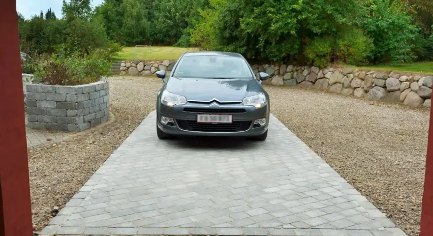 Grå bil parkerad på en vacker stenlagd uppfart. En fin uppfart inspiration med stenmur och grönska i bakgrunden.