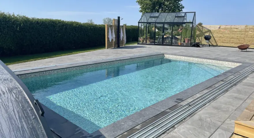 En vacker pool med mosaikdetaljer, perfekt för att bygga egen pool. Omgiven av en modern uteplats med växthus och dusch.
