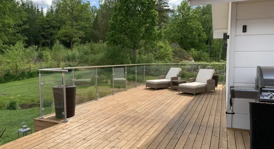 Solig altan med olja trall, solstolar och grill. Vacker utsikt över grönskande skog.