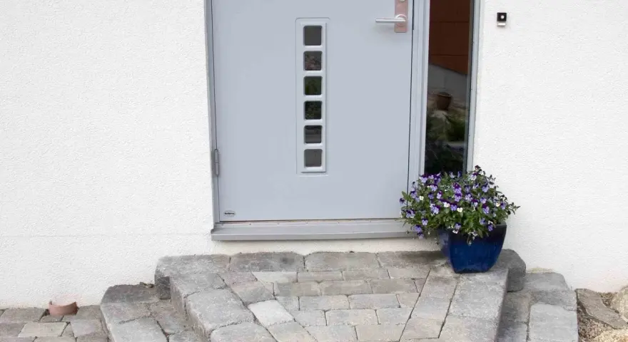 En vacker stentrappa leder upp till en modern ytterdörr. En blå kruka med blommor ger färg åt entrén.