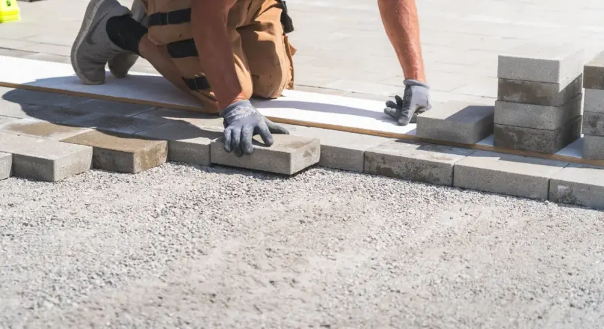 Arbetare lägger stenplattor för en ny uppfart. Grå betongplattor staplas och placeras noggrant på grus.