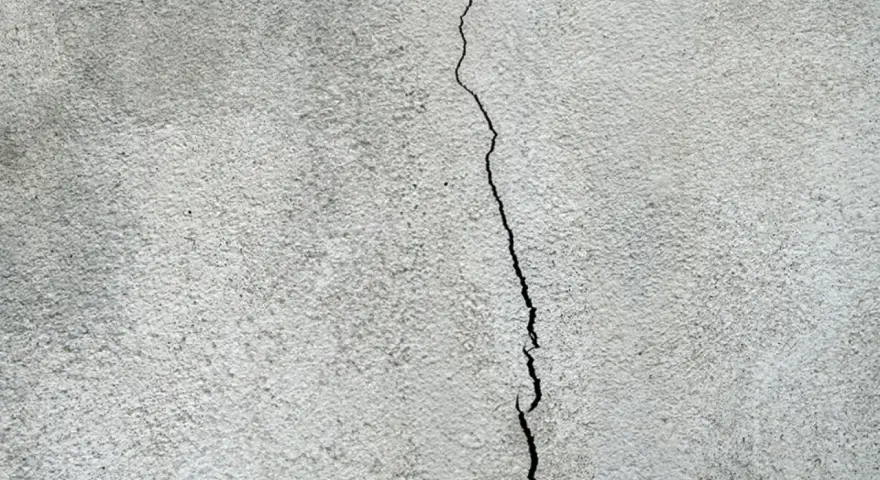 Spricka i en grå, putsad fasad. Dags att laga putsad fasad för att förhindra större skador.