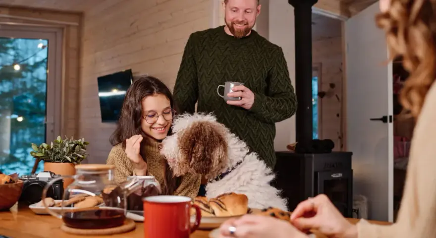 Familj med hund myser vid bordet med fika. Trots att det är lite dålig luft hemma, sprider sig värme och glädje.