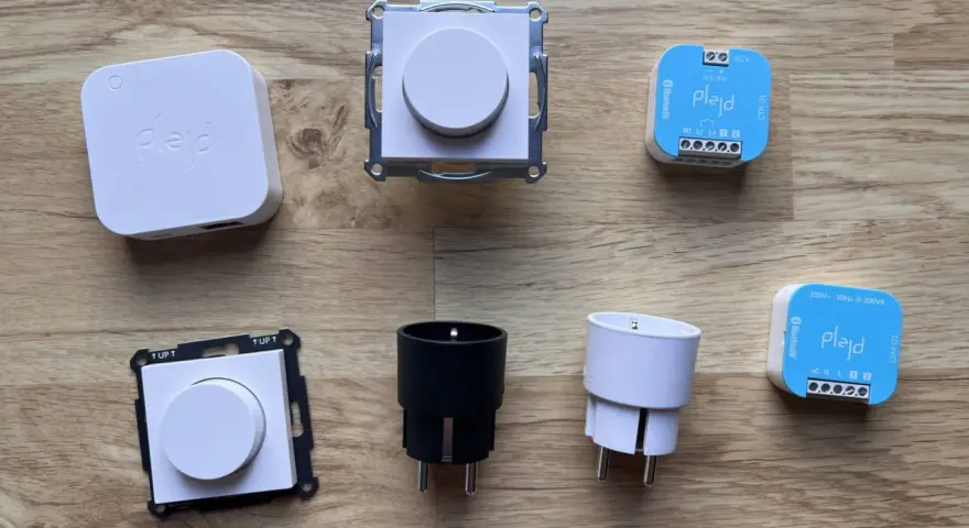 En samling Plejd-produkter, inklusive en vit Plejd-box, två dimmerknappar, två elkontakter och två styrenheter som stöder Plejd-protokoll.