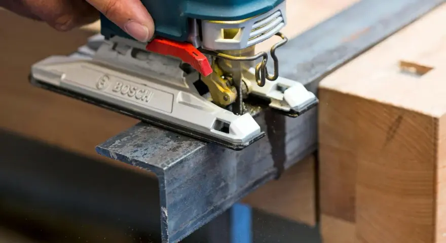 En hand använder en sticksåg för att såga snett i en metallprofil.