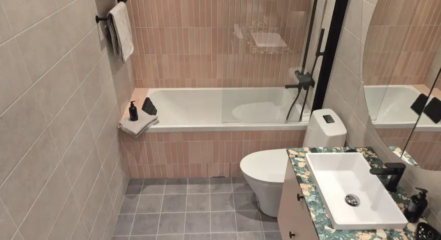 Ett modernt badrum med rosa kakel vid badkaret och grått klinkergolv. En vit toalett och ett handfat med en unik bänkskiva.