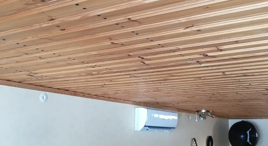 Ett vackert träpaneltak, redo att måla. En luftkonditionering och gitarrer syns nedanför.