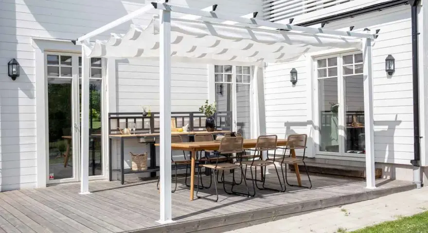 En vit pergola med tygtak skapar en mysig uteplats med matbord och stolar. Perfekt för att bygga pergola med plasttak för soliga dagar.