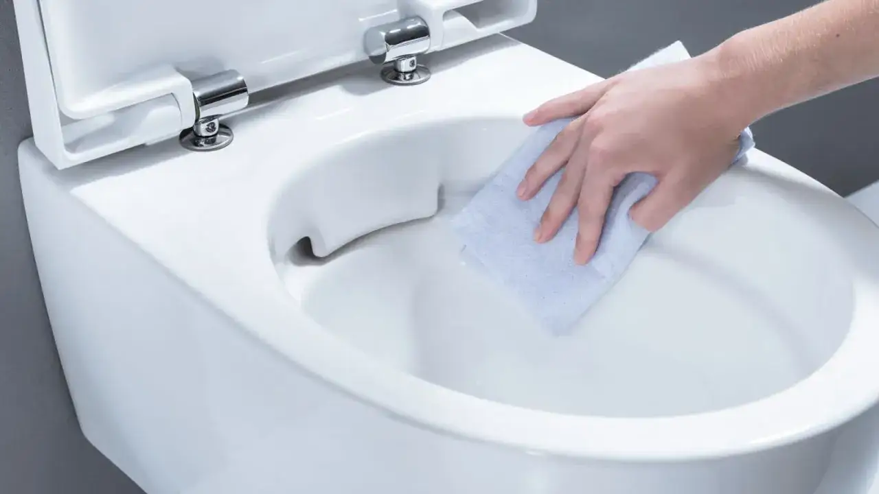 En hand torkar rent en snålspolande toalett med en blå trasa.
