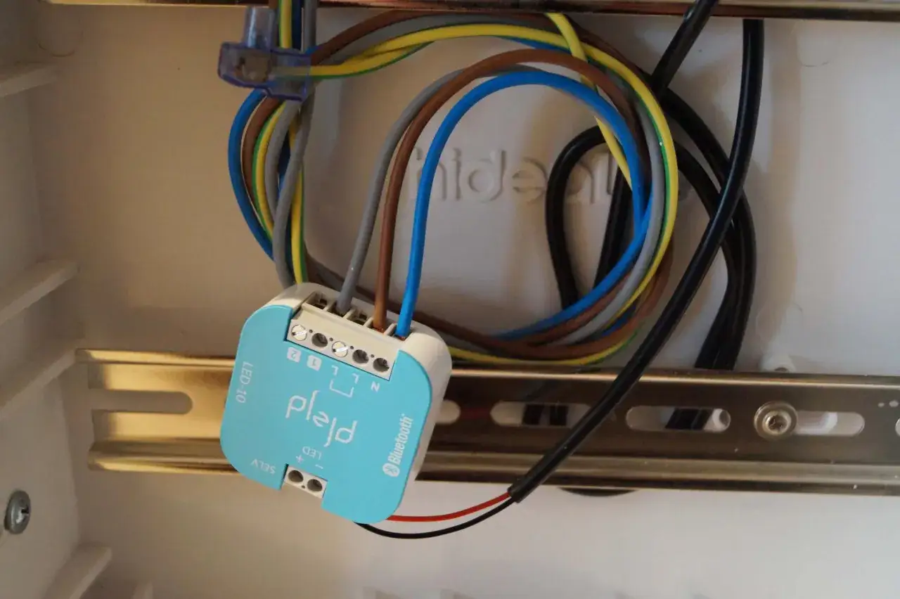 En blå Plejd-modul med Bluetooth är ansluten till flera färgglada kablar i en elcentral.