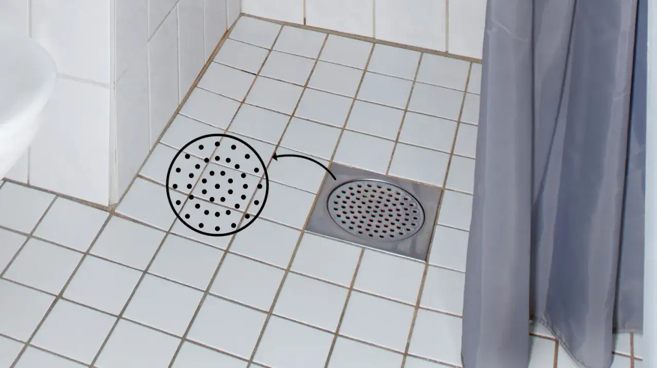 En närbild av ett duschgolv med vita kakelplattor och en metallgolvbrunn. En cirkel med prickar visar hur man kan rensa golvbrunn.