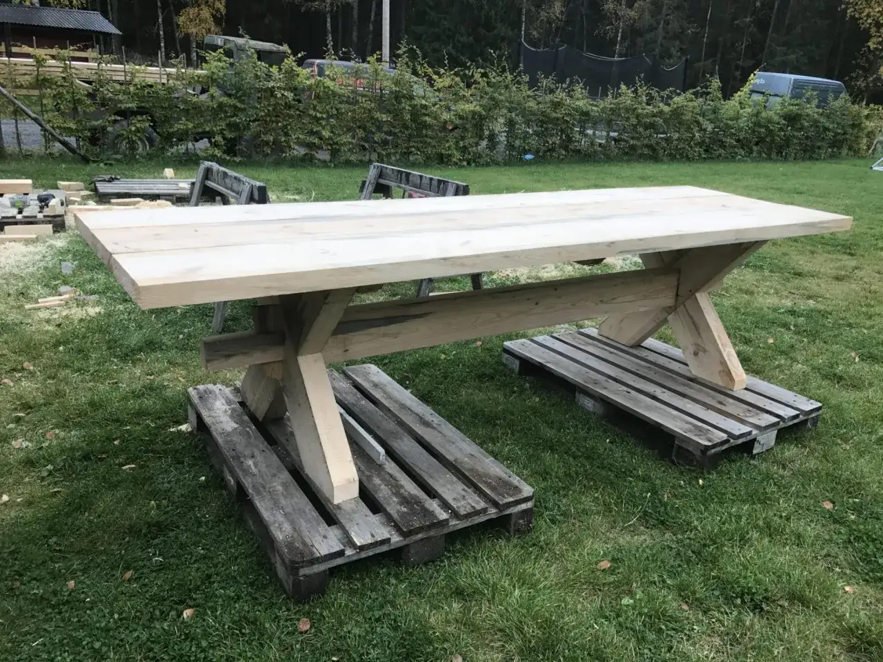 Ett grovt, hemmabyggt matbord i tr&auml; st&aring;r p&aring; pallar utomhus. Perfekt f&ouml;r den som vill bygga eget matbord.