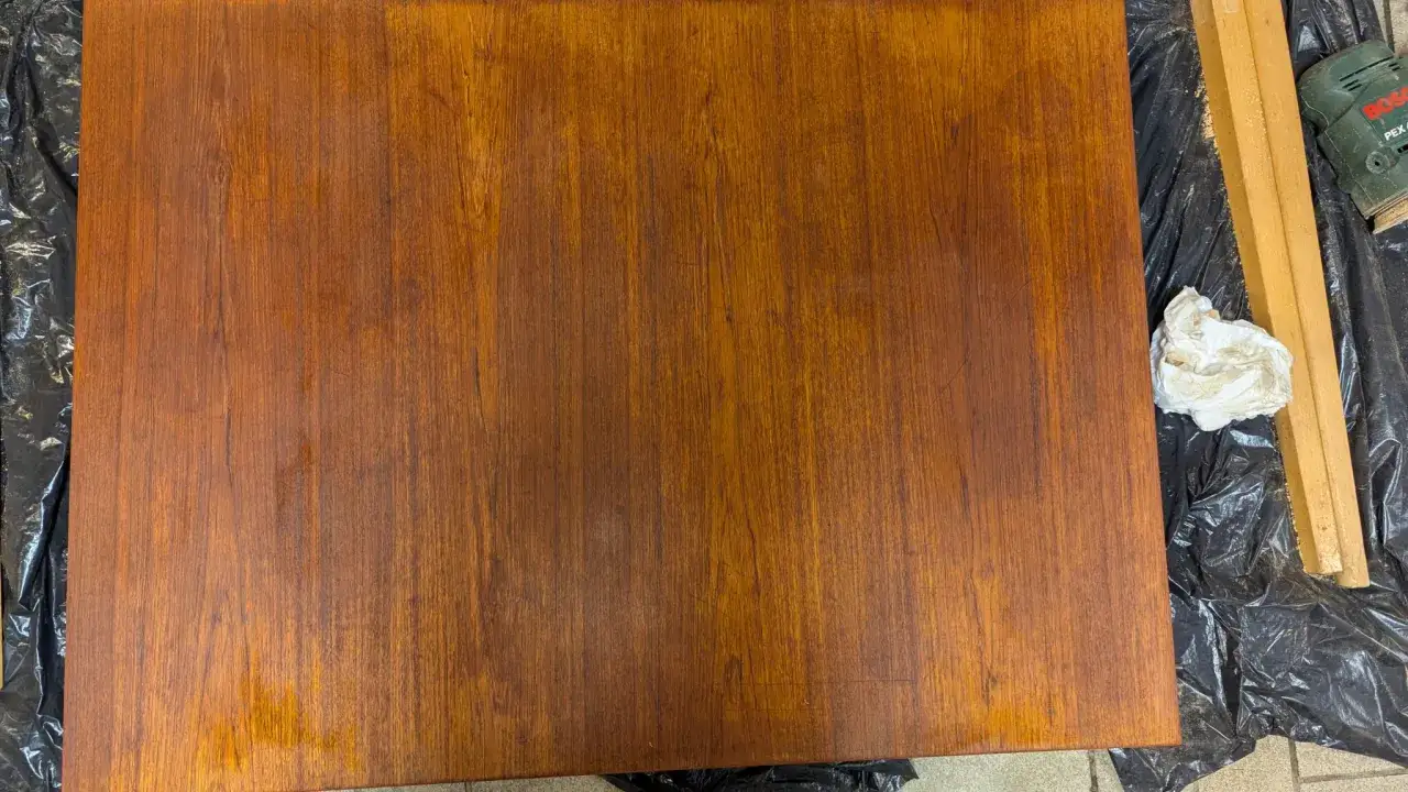 F&ouml;rbereder f&ouml;r att slipa teakbord. En bit tr&auml; ligger p&aring; svart plast, bredvid en slipmaskin och en pappersbit.