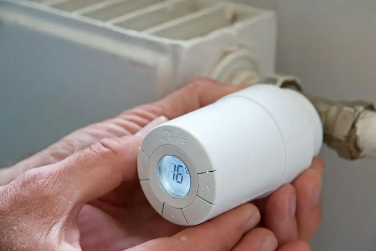 En hand justerar en vit radiator termostat med digital display som visar 18 grader.