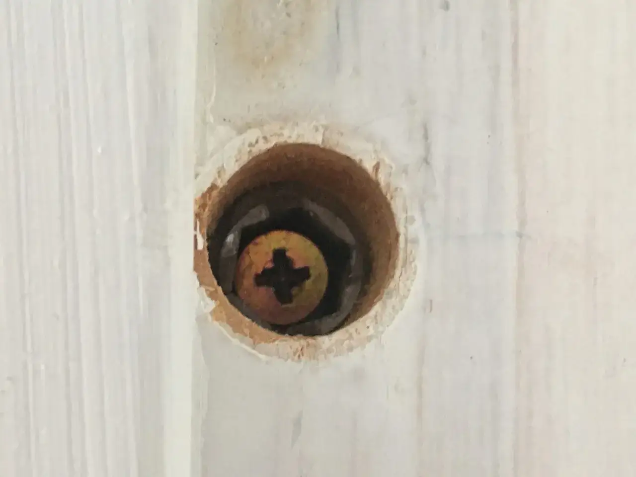 Detaljbild av ett hål i en vitmålad träkarm där en karmskruv syns.