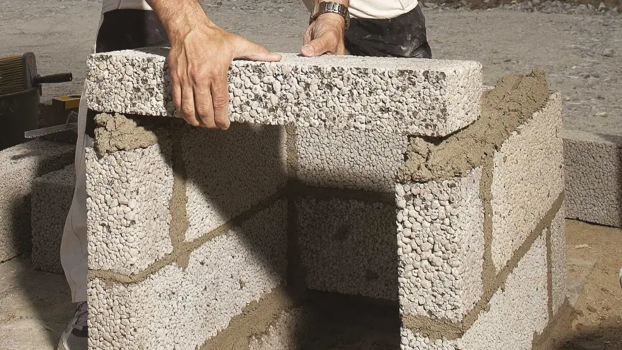 Händer lägger ett mura lecablock på en mur av lecablock med murbruk.