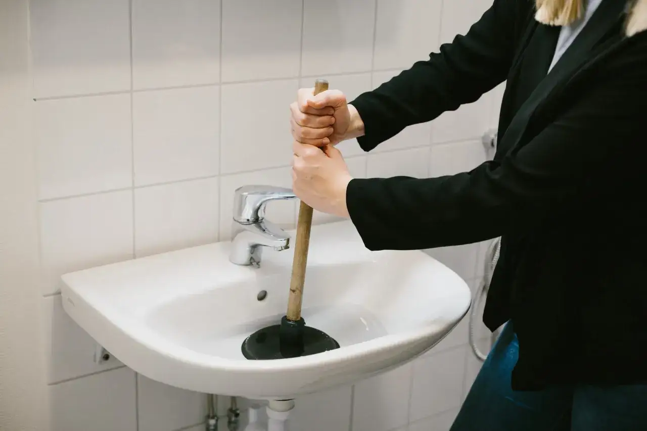 Person använder en sugpropp för att rensa vattenlås i handfatet.
