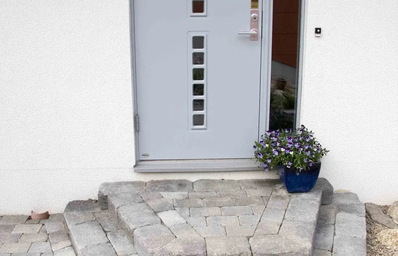 En vacker stentrappa leder upp till en modern ytterdörr. En blå kruka med lila blommor står vid sidan.