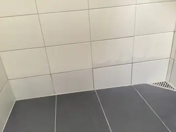 Fuktskada kakel i duschen. Mörka fläckar syns på de ljusa väggplattorna, ett tecken på fuktproblem.