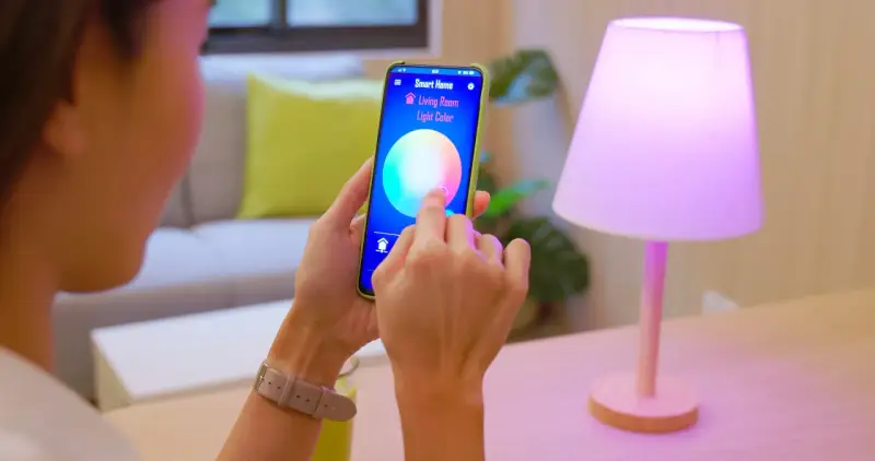 Person styr lampor med iPhone. Appen "Smart Home" visar färgval för vardagsrumsljuset.