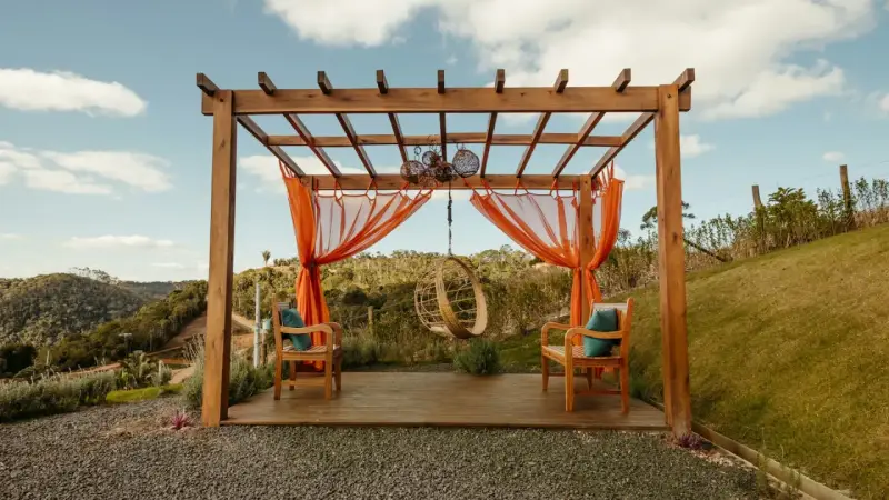 En vacker träpergola med orange draperier och hängstol. Perfekt för att bygga pergola på altan och njuta av utsikten.